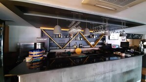 Un espace bar au design moderne, avec un comptoir en béton, des suspensions lumineuses et des étagères remplies de bouteilles et de verres.