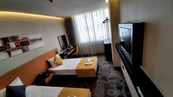 A hotel room with two beds, a desk, a TV, and a large window with curtains.