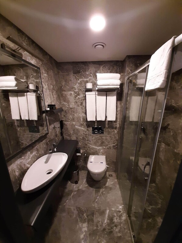 A modern bathroom with a marble floor, a sink, a toilet, and a glass shower enclosure.