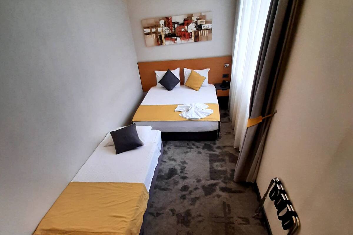 A hotel room with two beds, a desk with toiletries, a small table, and a wall-mounted shelf.