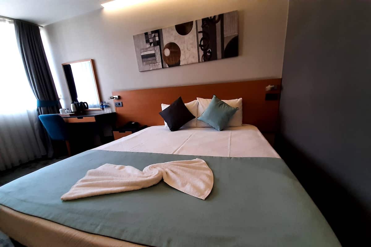 A hotel room with a neatly made bed, a desk with a chair, and a painting on the wall.