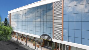 Un hôtel moderne doté d’une grande façade en verre, d’un espace extérieur aménagé et d’une enseigne indiquant « HÔTEL SAPKO AÉROPORT ».