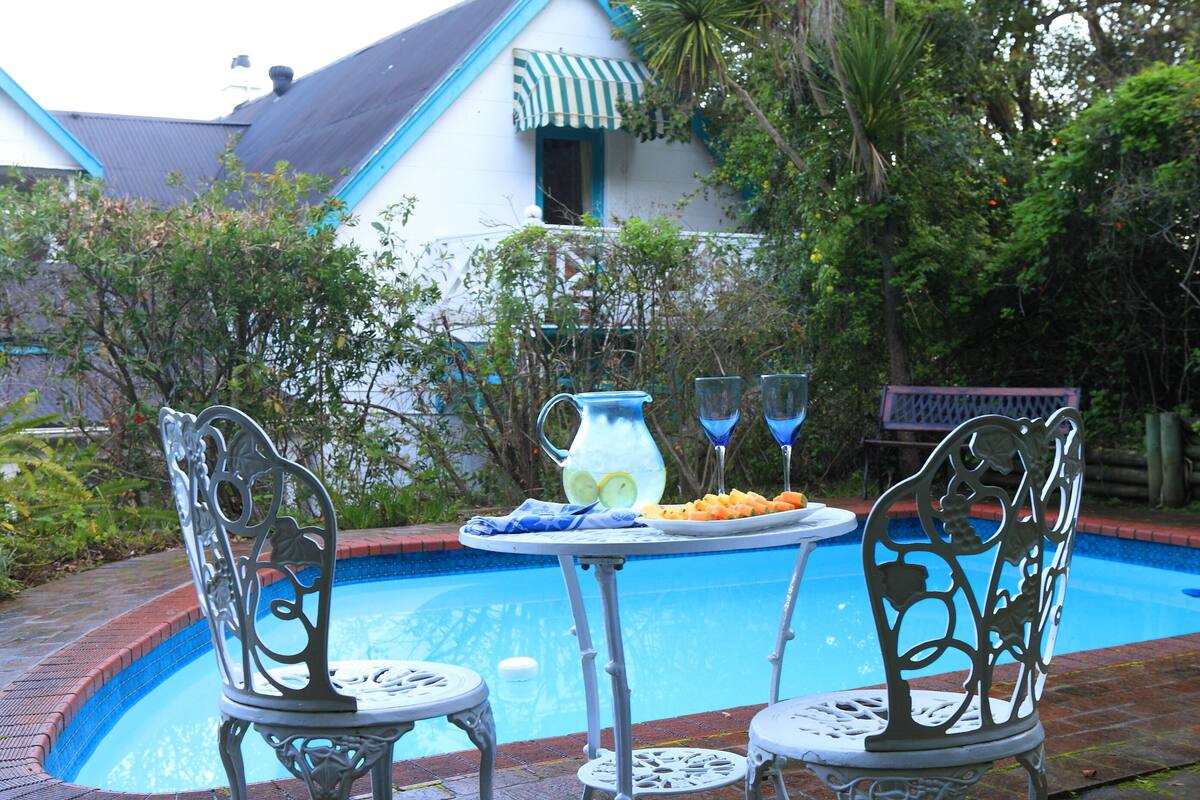 A poolside setting with a table and chairs, a pitcher, and a plate of food.