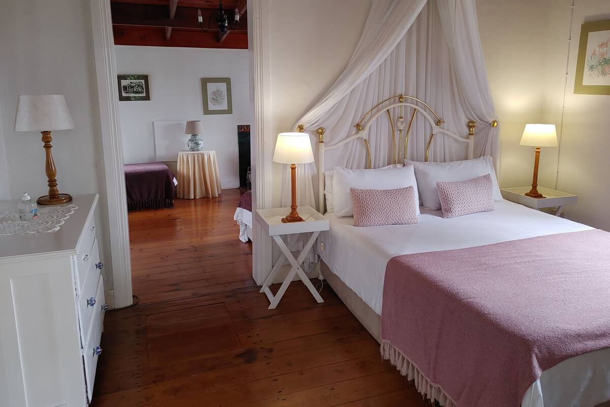 A bedroom with a four-poster bed, two bedside tables with lamps, a wooden floor, and a white wardrobe.