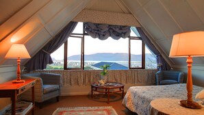 A cozy room with a bed, two chairs, a small table, and a window with a view of a cityscape. - Yellowwood Lodge - Adults Only (Knysna)