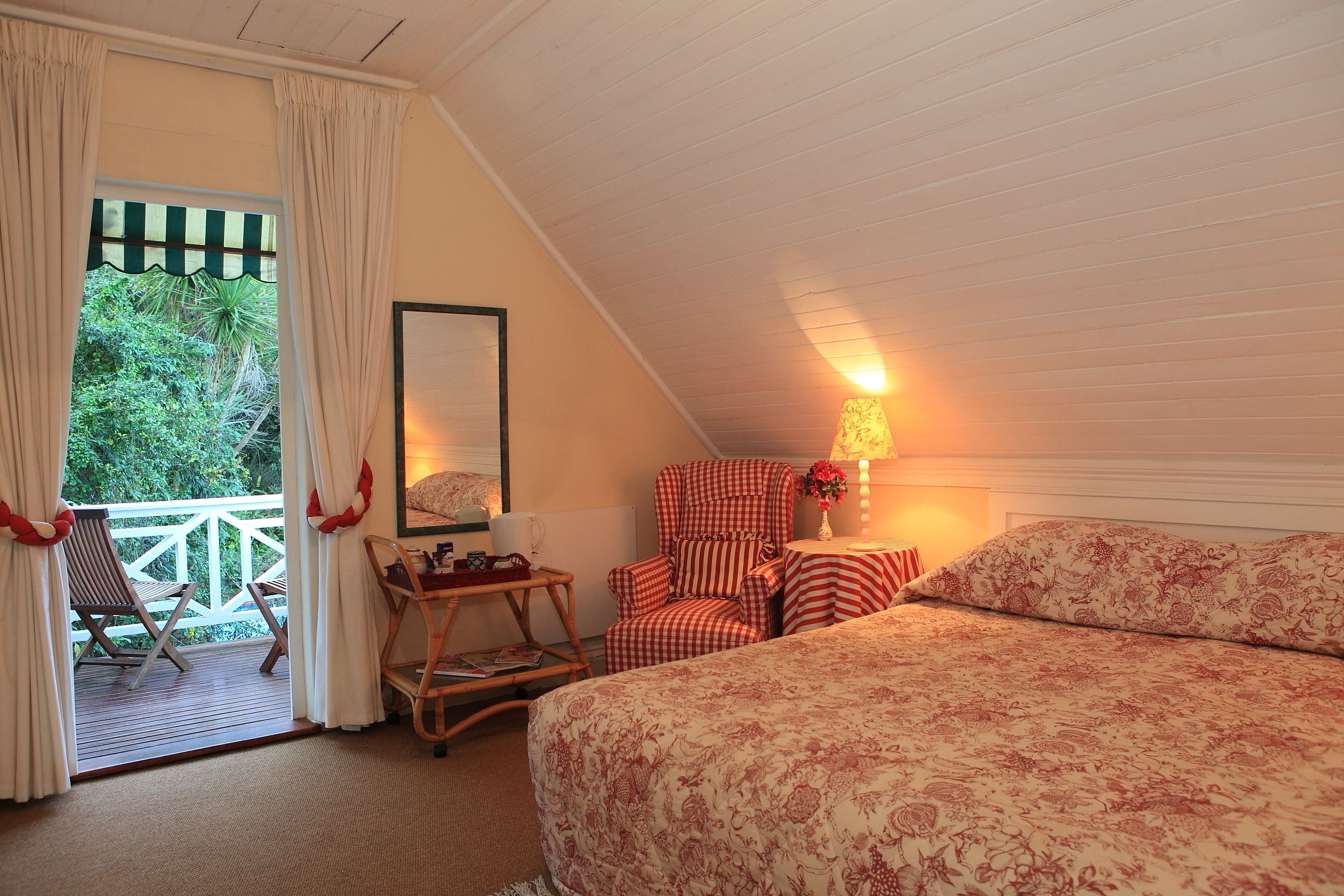 A cozy bedroom with a bed, a chair, a small table, and a balcony with a view of greenery.