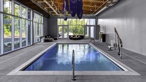 An indoor swimming pool with clear glass walls, a wooden ceiling, and a view of the outdoors.