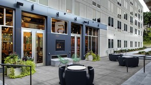 An outdoor seating area with modern furniture, a building entrance with glass doors, and a well-maintained garden.