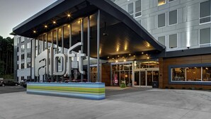 A modern hotel entrance with a large sign, a covered walkway, and a parking area.