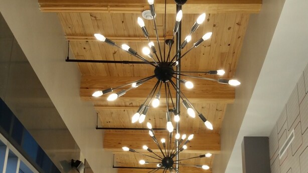 A hallway with a modern chandelier, wooden ceiling beams, and large windows.
