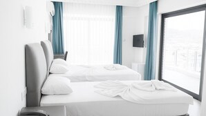 Habitación de hotel con dos camas, una mesita de noche con teléfono, un televisor montado en la pared y un ventanal con cortinas.