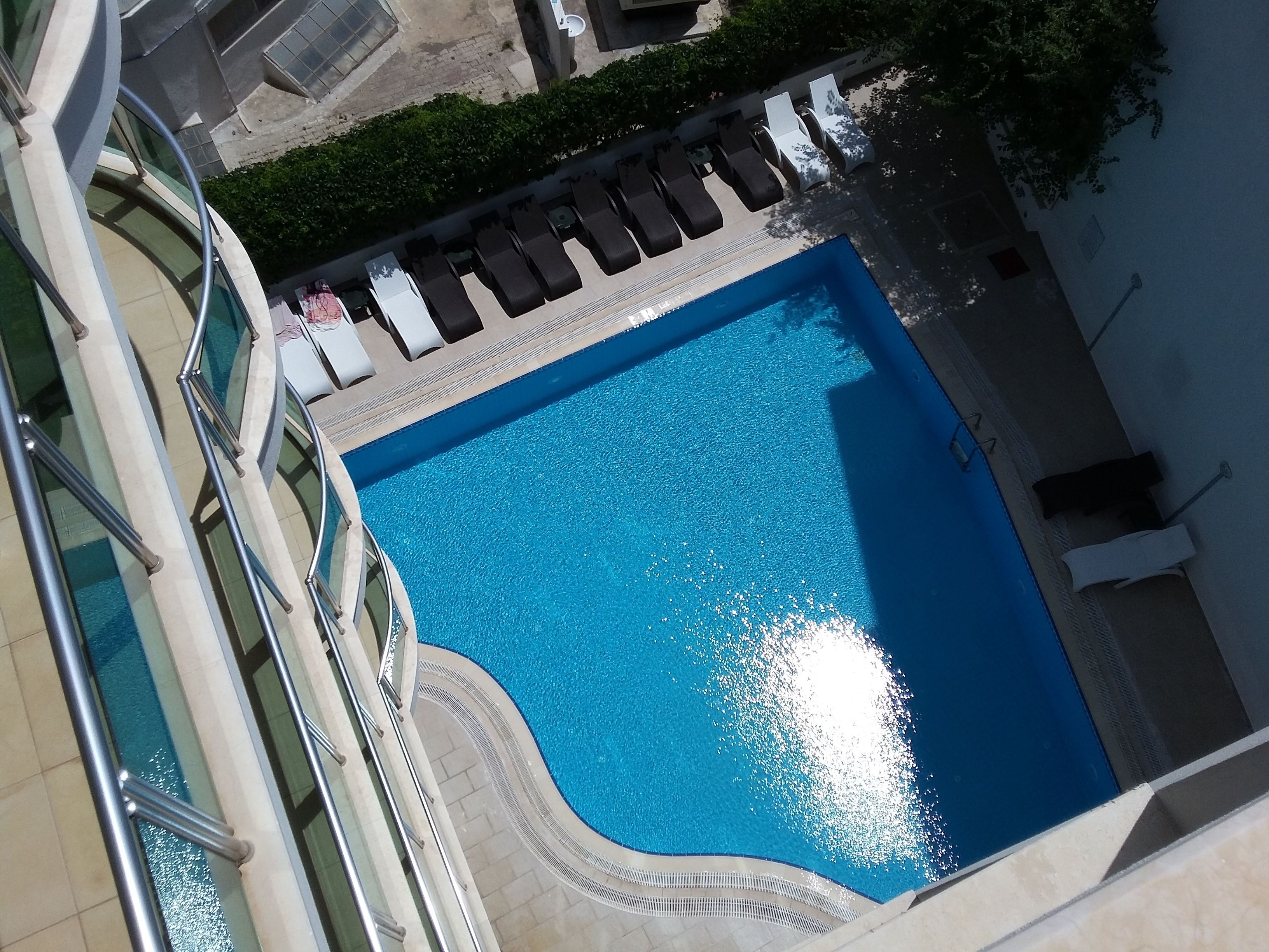 A large, clear blue pool with a curved edge, surrounded by a tiled deck and a metal railing.