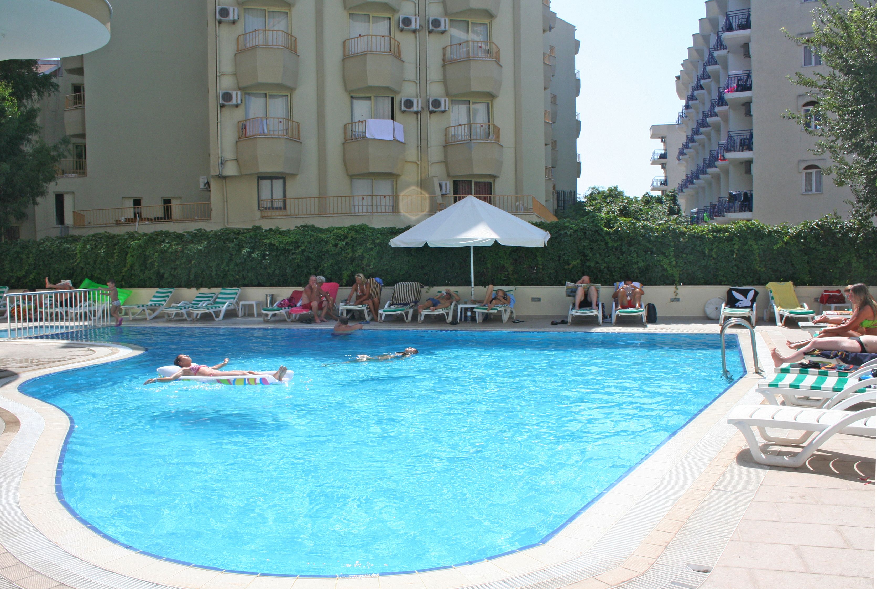A swimming pool with lounge chairs and umbrellas, surrounded by apartment buildings.