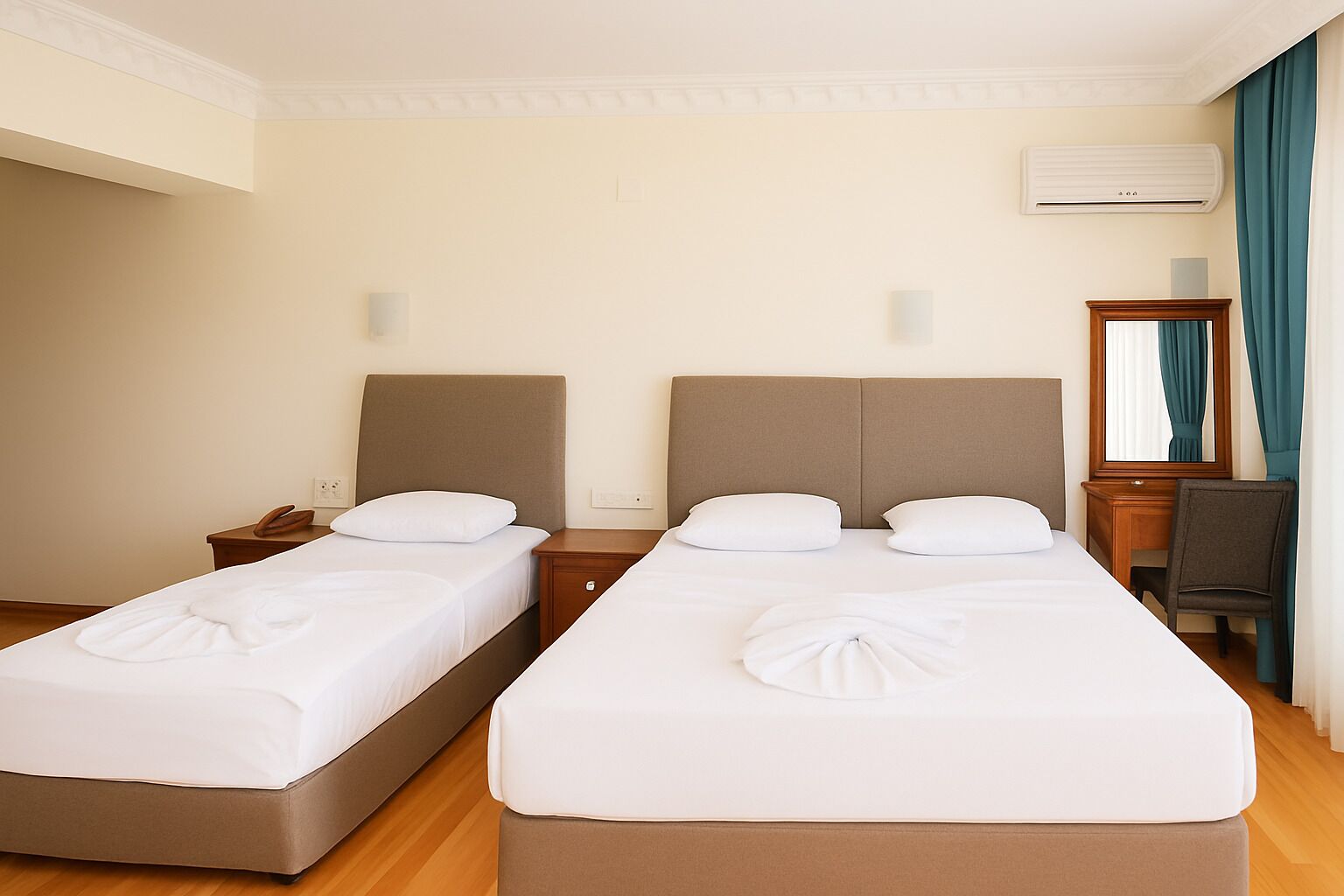 A hotel room with two single beds, a wooden nightstand with a phone, a desk with a chair, and a mirror.