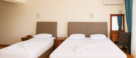 A hotel room with two single beds, a wooden nightstand with a phone, a desk with a chair, and a mirror.
