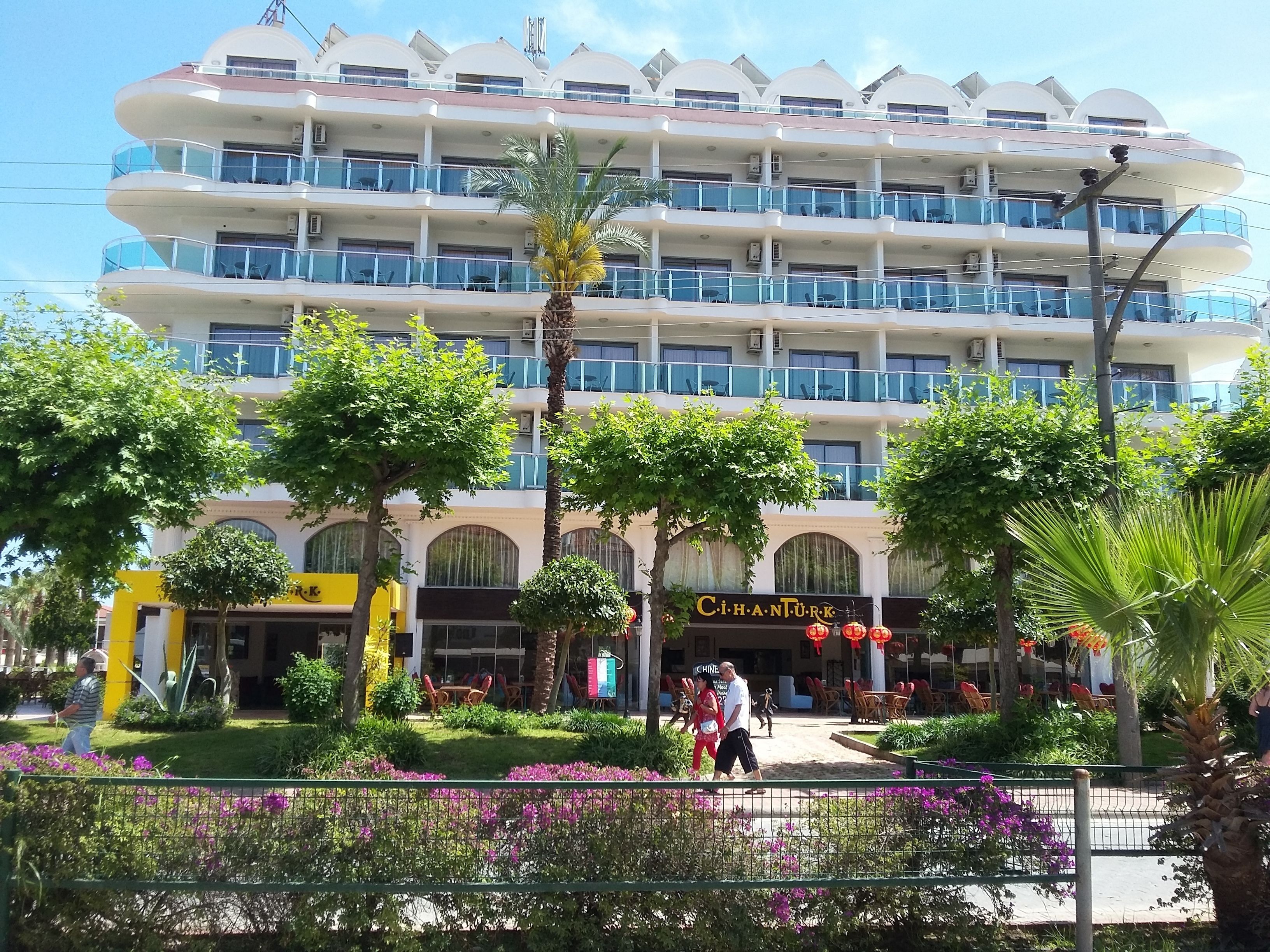A multi-story hotel with balconies, a central courtyard with seating, and a restaurant named "CihanTürk".