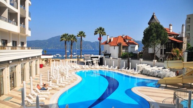 A resort pool with lounge chairs, palm trees, and a view of the sea. - Golden Rock Beach Hotel - All Inclusive (Marmaris)