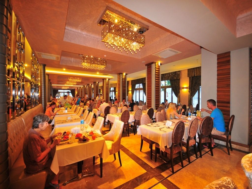A restaurant with multiple dining tables and chairs, a bar area with bottles, and a chandelier.