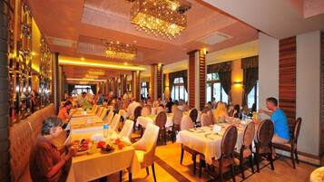 A restaurant with multiple dining tables and chairs, a bar area with bottles, and a chandelier.