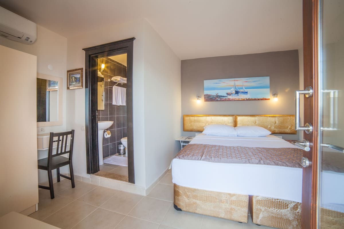 A hotel room with a bed, a desk, a chair, a bathroom, and a painting on the wall.