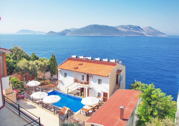A building with a swimming pool, outdoor seating, and a view of the sea. - Sunset Villa Hotel (Kas)