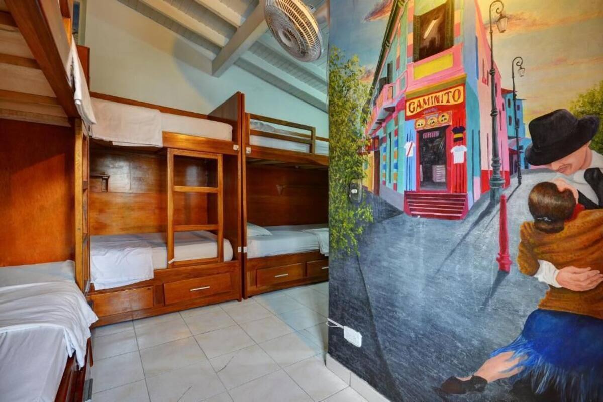 Una habitación con literas, un mural de una calle colorida y un ventilador en el techo.