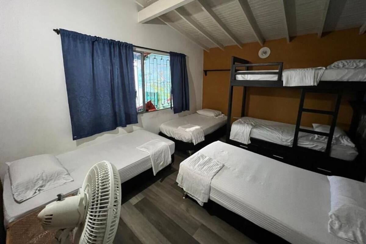 Un dormitorio con literas, una ventana con cortinas, un ventilador de pie y una pequeña mesa.
