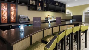 Zona bar moderna con un bancone curvo, sgabelli da bar e una varietà di bottiglie.