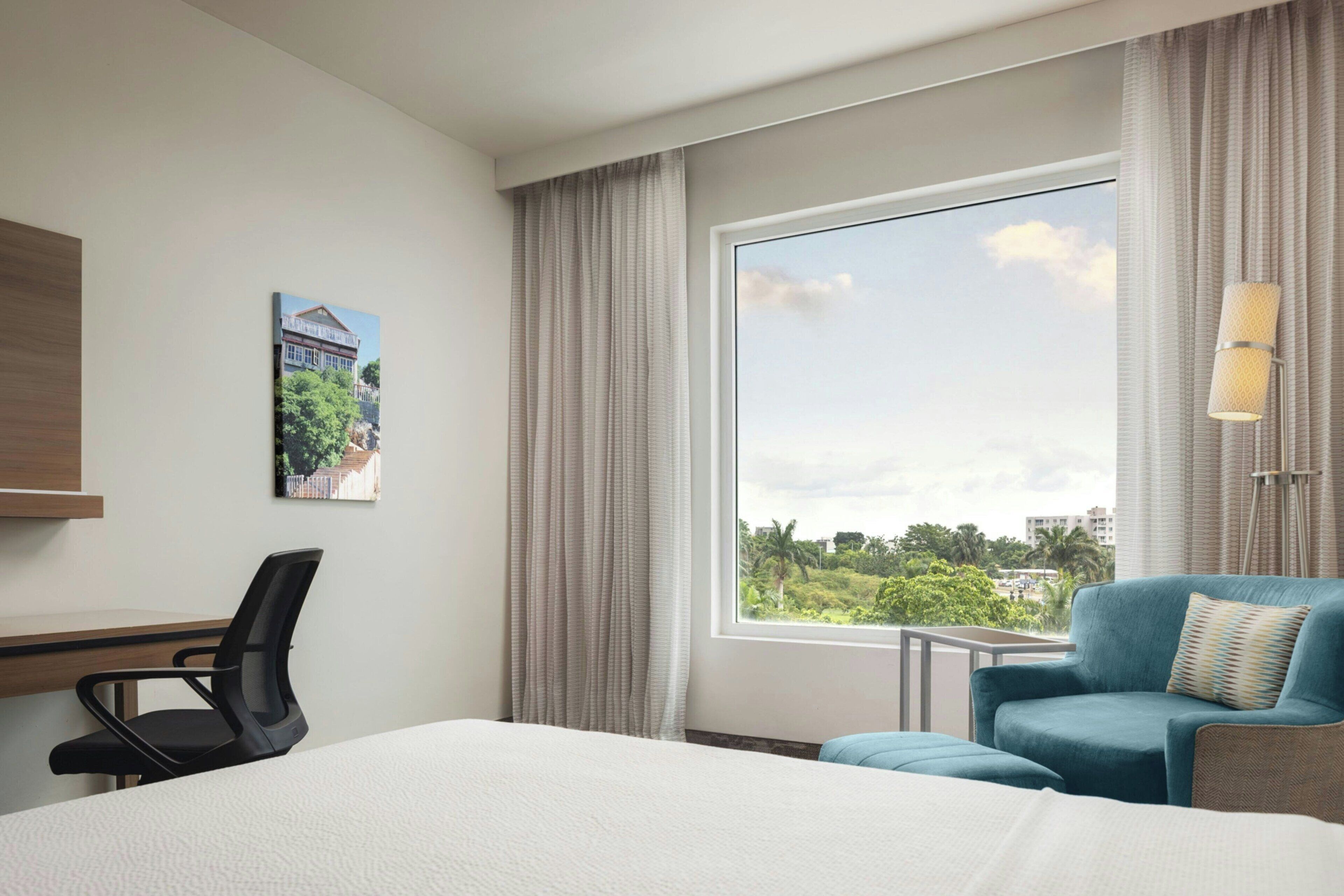 A hotel room with a large window, a bed, a desk, and a chair.