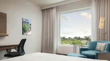 A hotel room with a large window, a bed, a desk, and a chair.