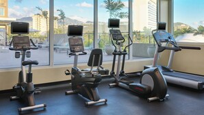Una palestra con macchinari cardio e tapis roulant, ampie finestre che offrono vista su palme e edifici.