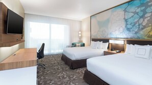Quarto de hotel com duas camas, uma escrivaninha, uma cadeira, televisão e um grande quadro abstrato na parede.
