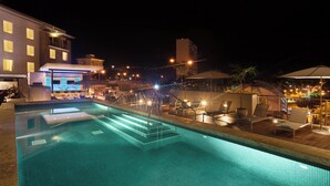 Area piscina illuminata di notte, con poltronne da relax e un angolo bar.