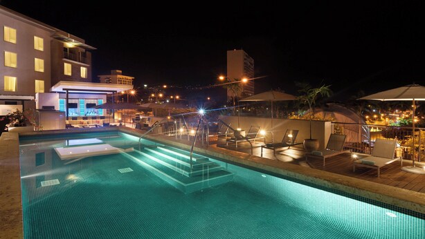 A nighttime swimming pool area with lounge chairs and a bar area. - Courtyard by Marriott Kingston, Jamaica (Kingston)
