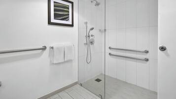 Une salle de bain moderne avec une douche à parois de verre, des barres d’appui, un porte-serviettes et un tableau encadré au mur.