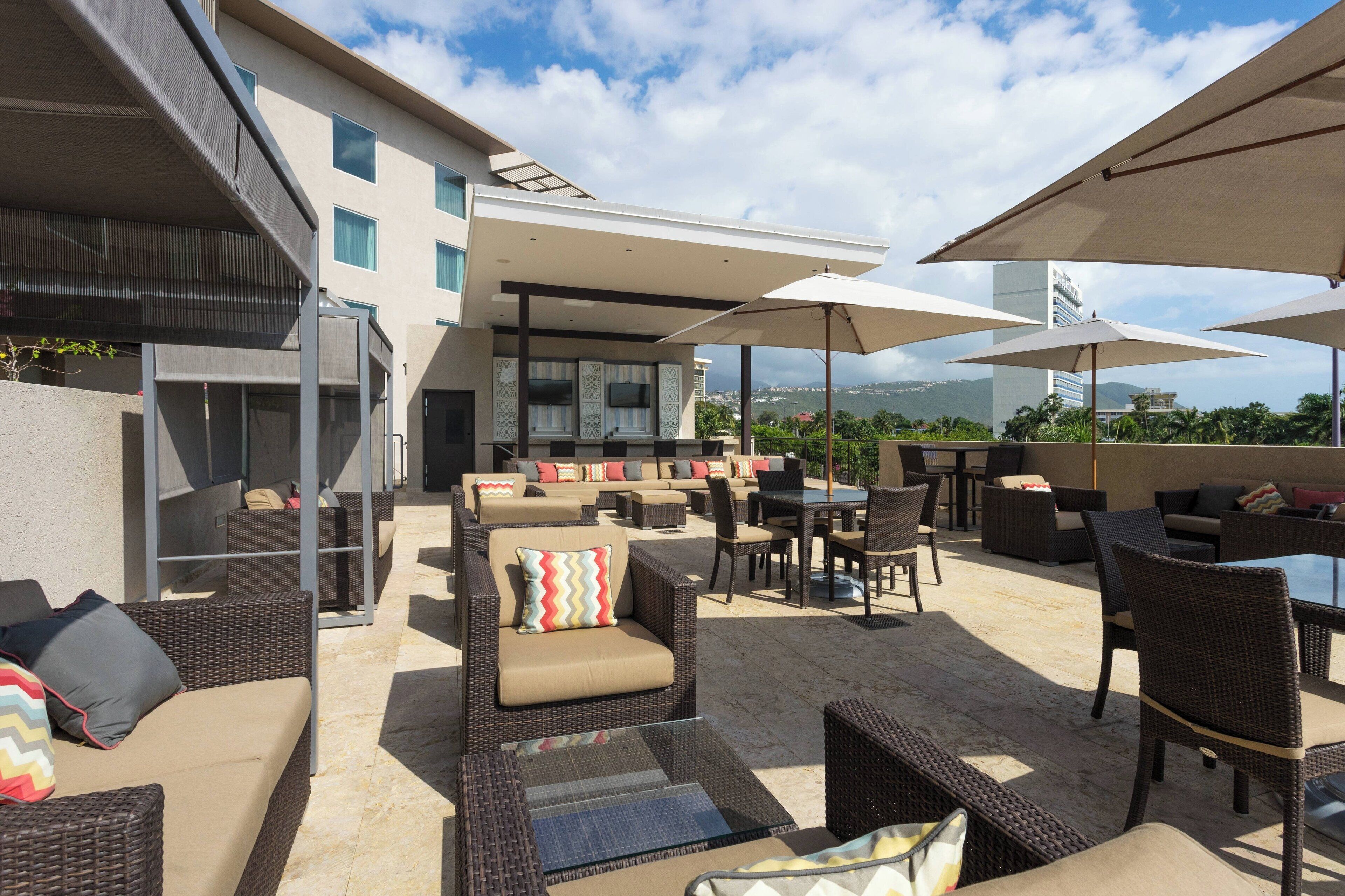 An outdoor patio area with wicker furniture, umbrellas, and a view of a cityscape.