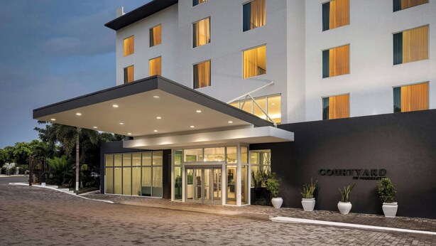 A modern hotel entrance with a covered walkway, glass doors, and potted plants. - Courtyard by Marriott Kingston, Jamaica (Kingston)