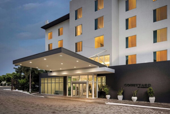 A modern hotel entrance with a covered walkway, glass doors, and potted plants. - Courtyard by Marriott Kingston, Jamaica (Kingston)