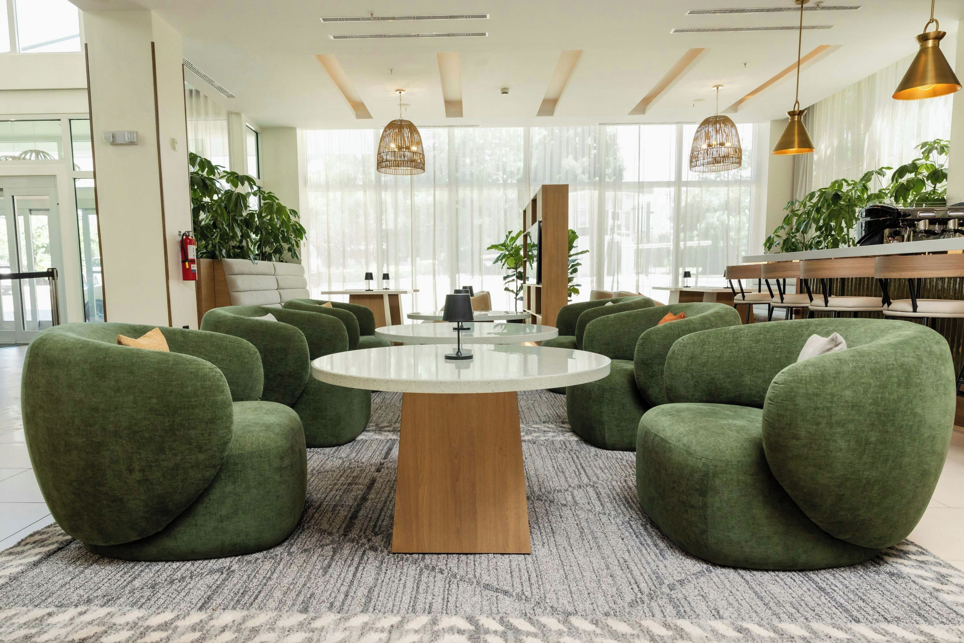 A modern interior with a round table surrounded by green chairs, a wooden coffee table, and pendant lighting.