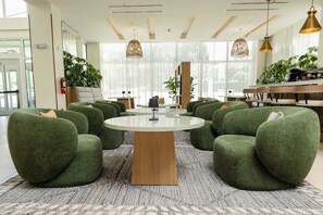 A modern interior with a round table surrounded by green chairs, a wooden coffee table, and pendant lighting. - Courtyard by Marriott Kingston, Jamaica (Kingston)