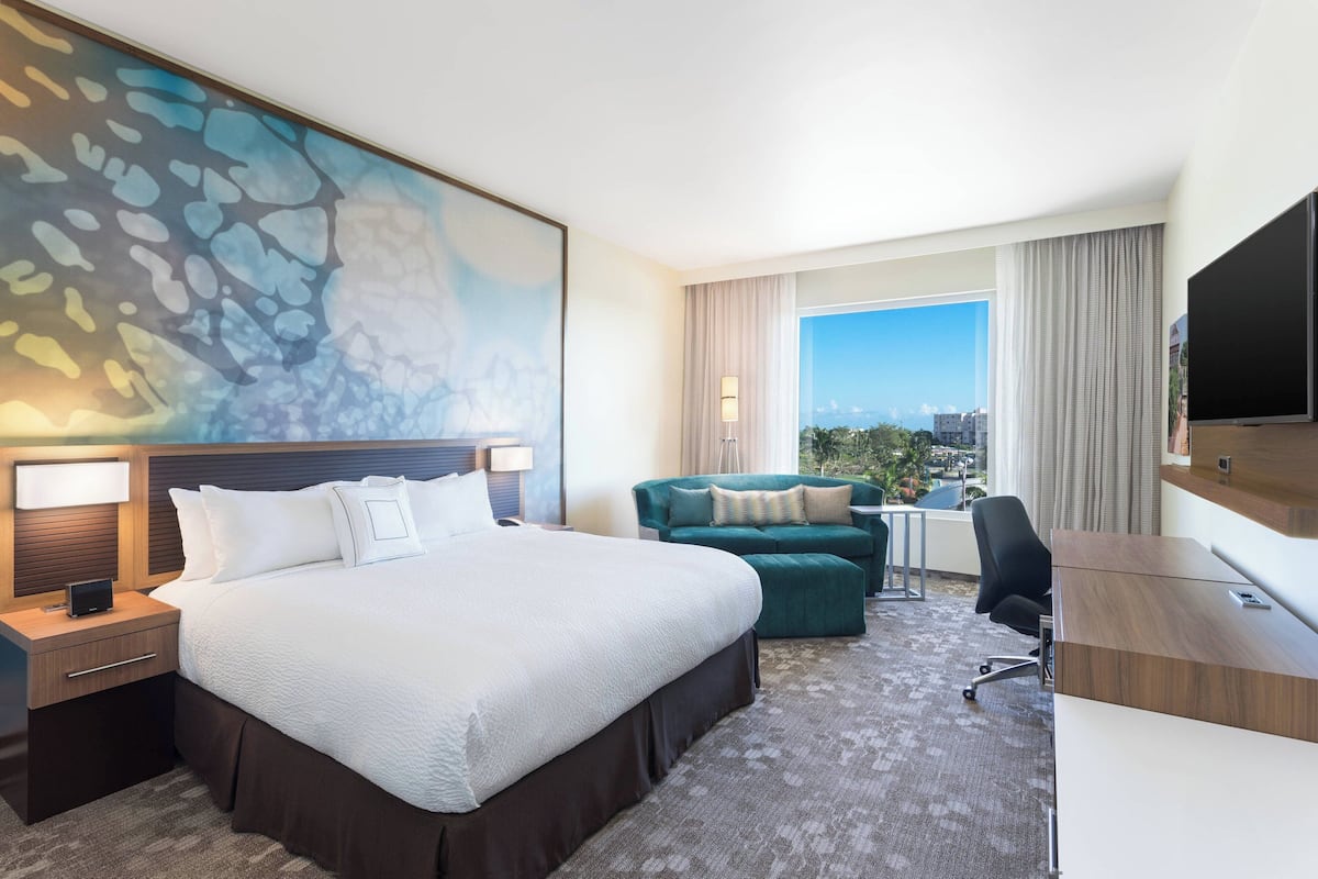 A hotel room with a large bed, a desk, a chair, a sofa, and a TV.