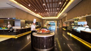 Un moderno vestíbulo de hotel con una isla central que ofrece mariscos, dos chefs trabajando y un piso elegante y pulido.