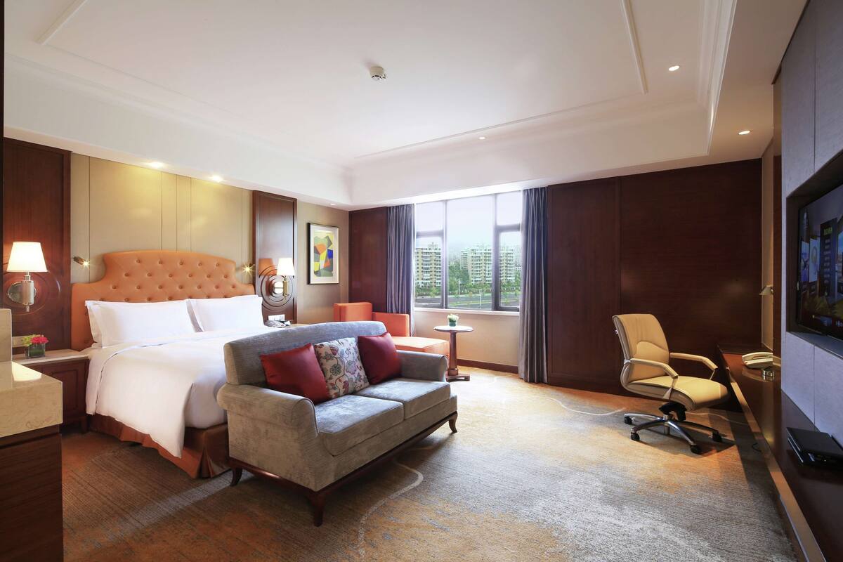 Una habitación de hotel con una cama grande, un sofá, un escritorio y una televisión.