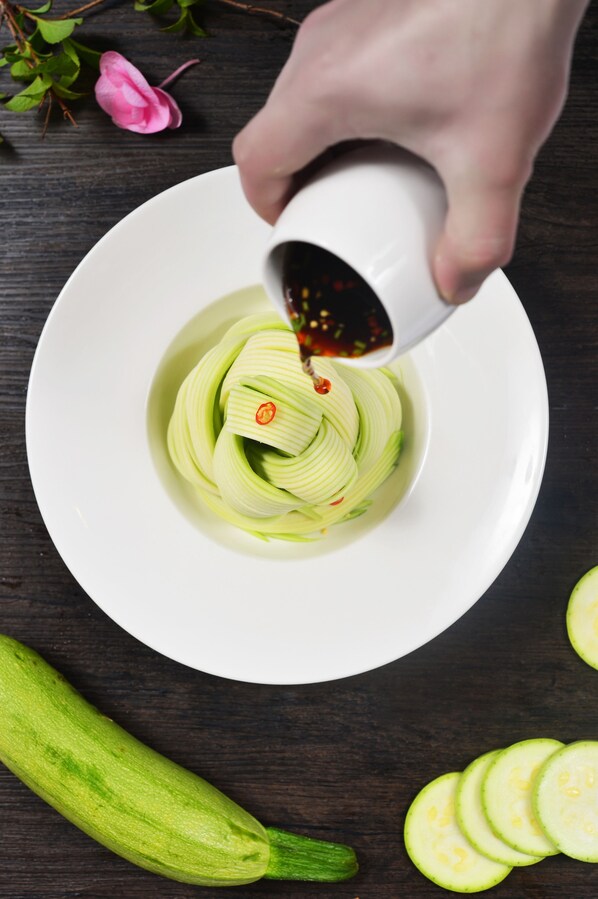 A hand pouring sauce over sliced cucumbers in a bowl. - Doubletree By Hilton Ningo - Chunxiao (Ningbo)