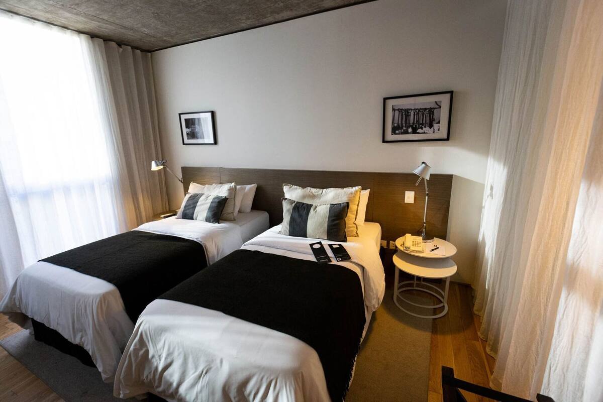 A hotel room with two beds, a bedside table with a lamp, a phone, and a framed picture on the wall.