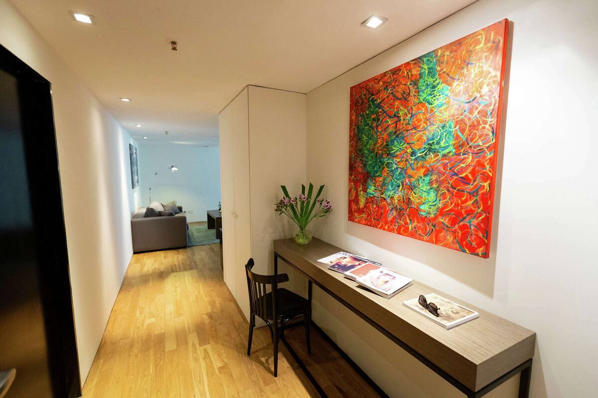 A hallway with a wooden floor, a desk with a vase of flowers, and a colorful abstract painting on the wall.