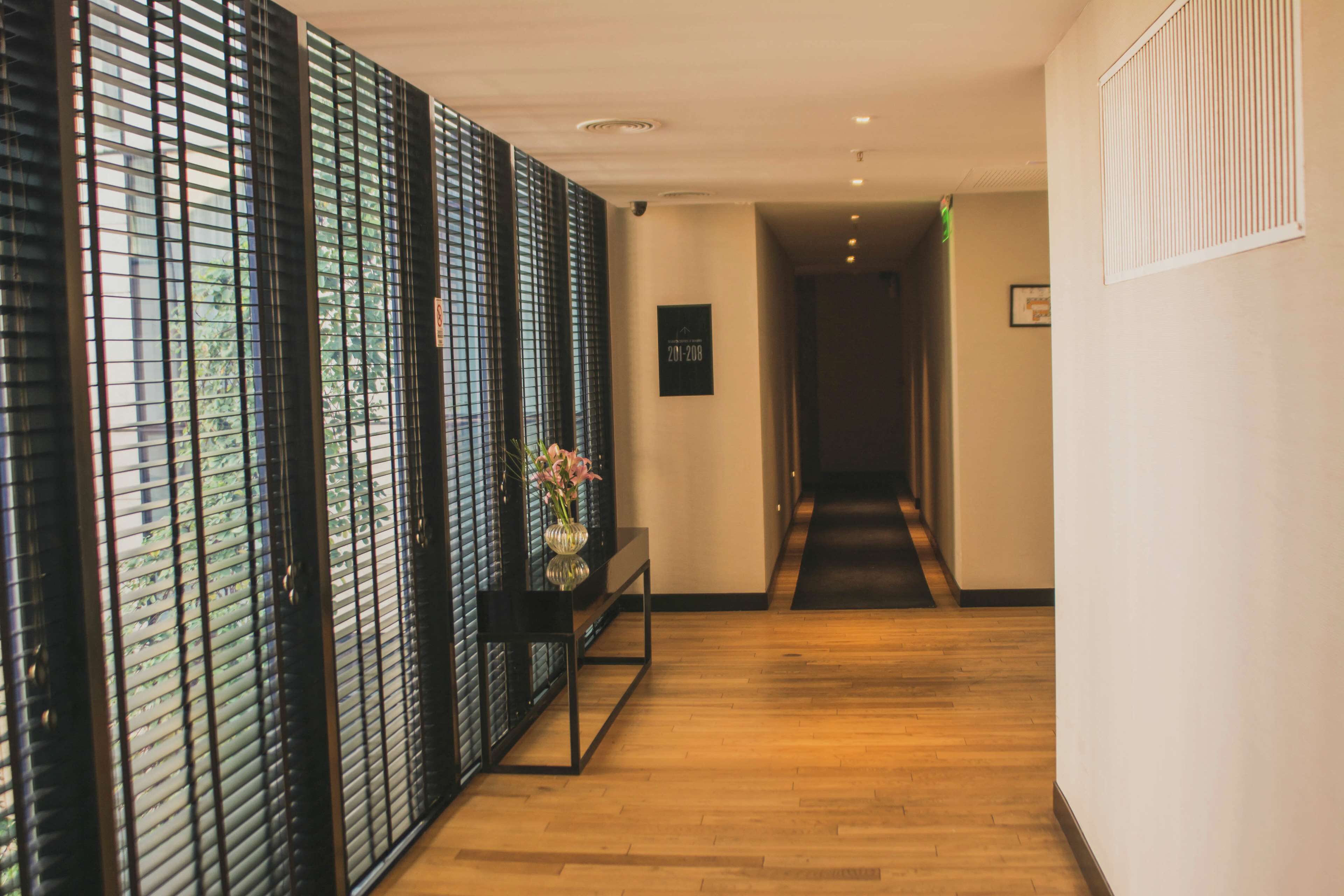 A hallway with wooden flooring, a black-framed mirror, and a vase with flowers on a console table.