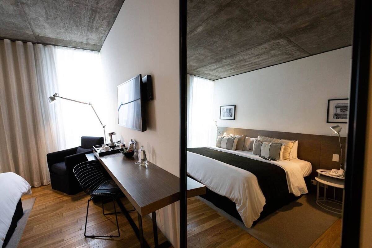 A hotel room with a bed, bedside table, desk, chair, lamp, and a TV mounted on the wall.
