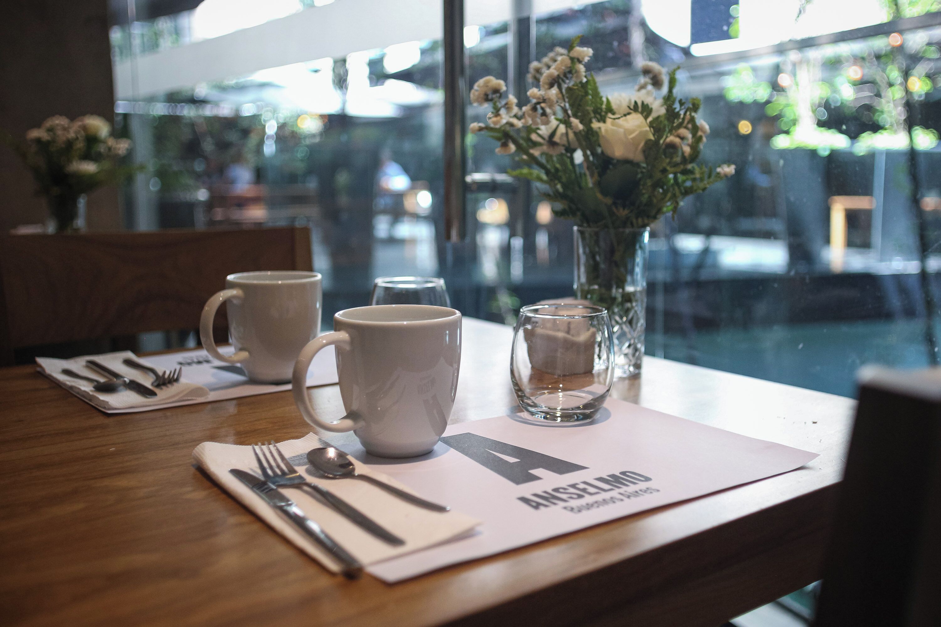 A table set with a white mug, a glass, a spoon, and a fork on a placemat with a letter 'A' and text.