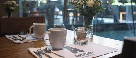 A table set with a white mug, a glass, a spoon, and a fork on a placemat with a letter 'A' and text.